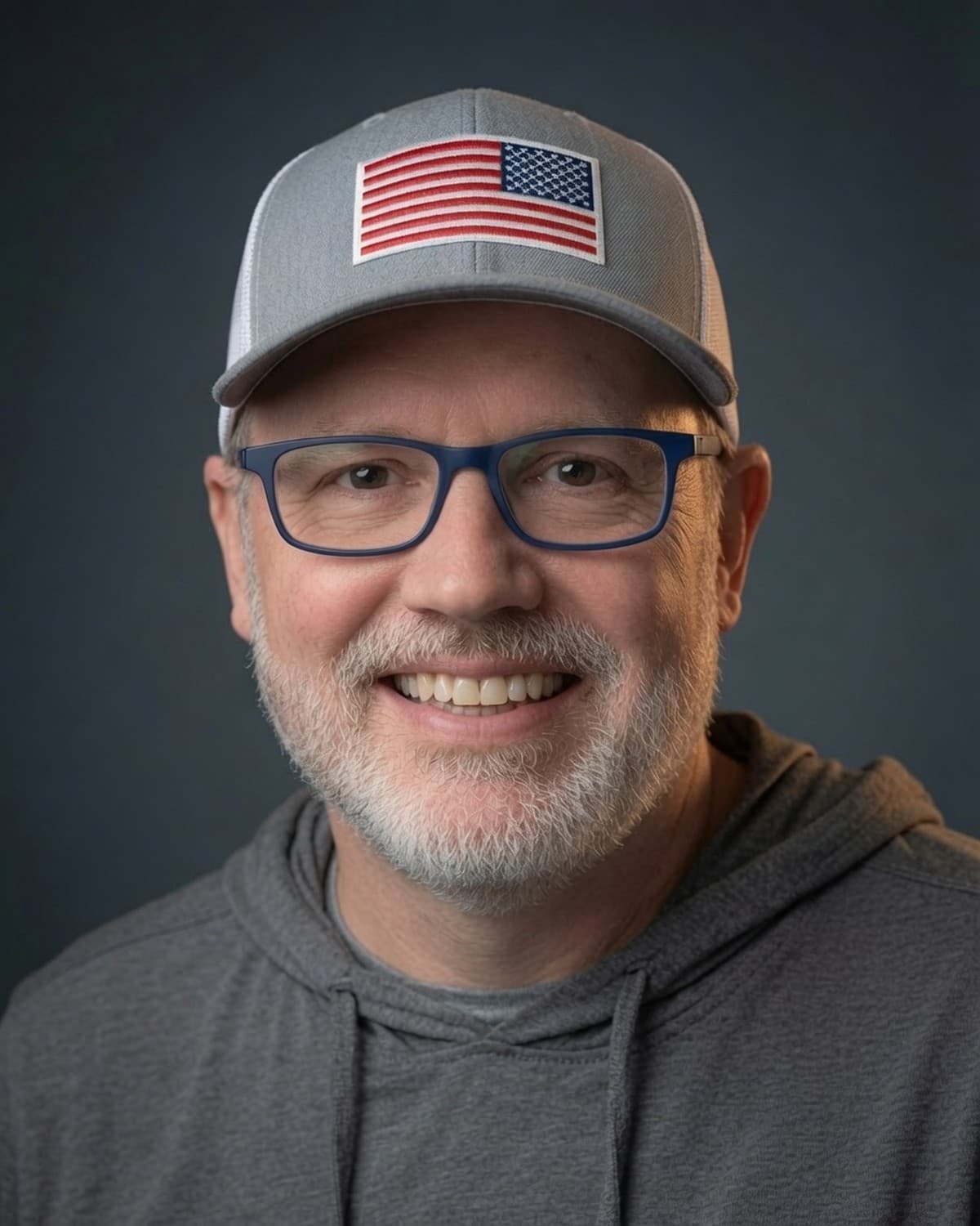 David Wilson — founder of Brand Forge Creative — studio portrait, gray cap, blue glasses, gray hoodie.